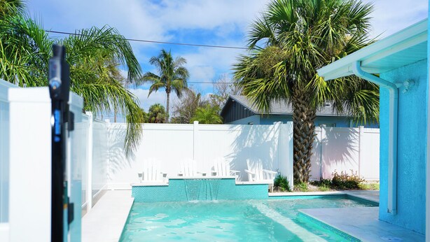 A swimming pool with clear water, surrounded by a white fence and palm trees.