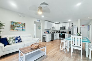 A modern living room with a white sofa, a coffee table, and a dining area with a table and chairs. - 4bd Duplex 1 blk from bch, pool Hot Tub, golf cart (Indian Rocks Beach)