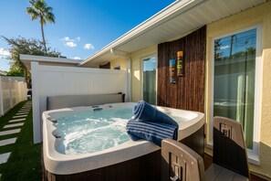 Un bain à remous avec une serviette à proximité, une terrasse en bois, une clôture blanche et un palmier.