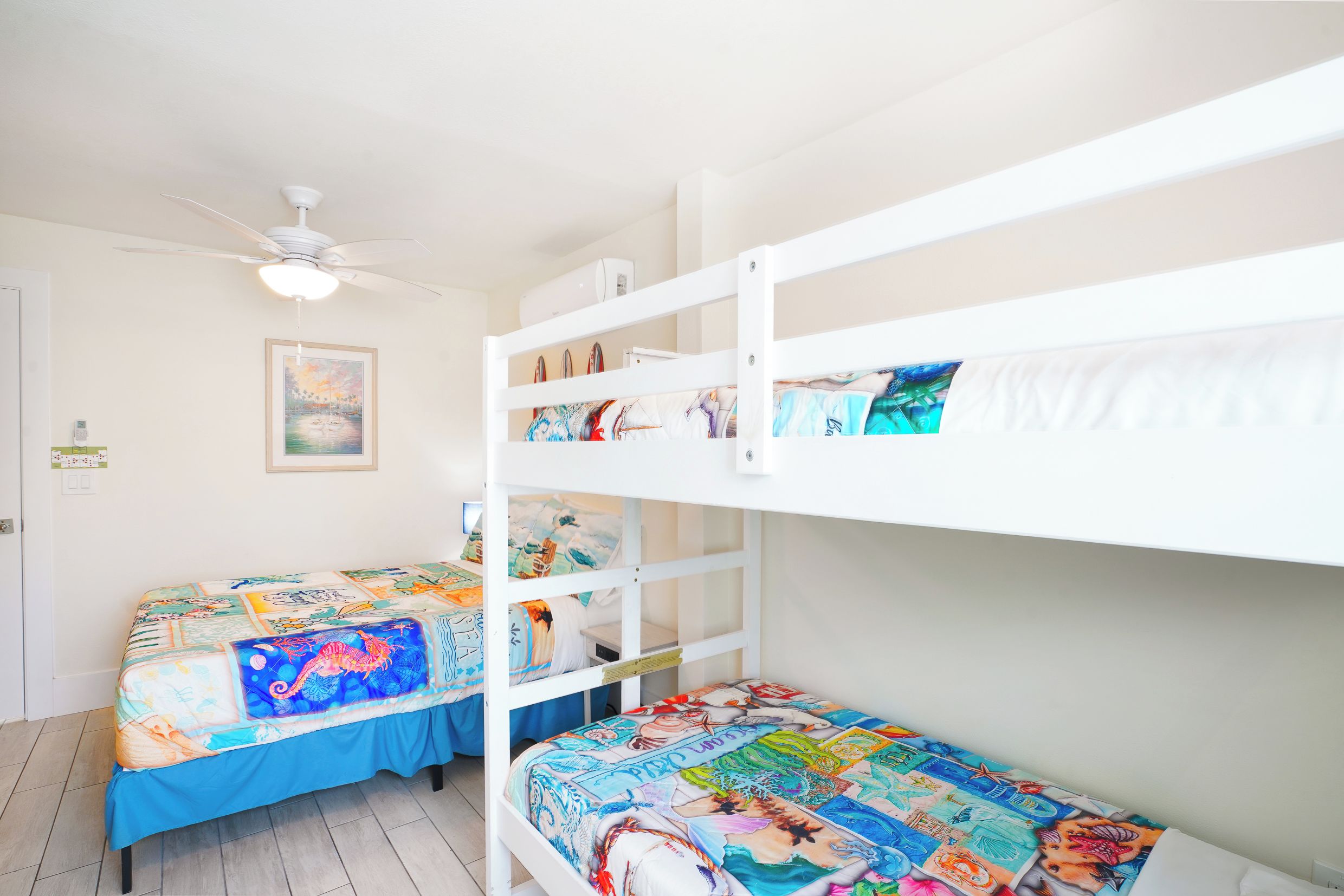 A bunk bed room with a ceiling fan, a framed picture on the wall, and a bed with a colorful quilt.