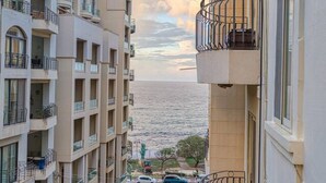 Un edificio residencial de varios pisos con balcones que dan a una calle y una masa de agua.