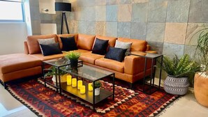Ein Wohnzimmer mit einem Ecksofa, einem Glastisch und einem gemusterten Teppich.