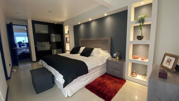 Ein modernes Schlafzimmer mit einem großen Bett, einem Nachttisch, einem roten Teppich und integrierten Regalen mit Dekoration.