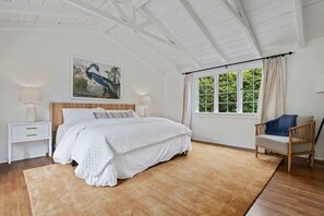 A bedroom with a large bed, a nightstand, a chair, and a window with curtains.