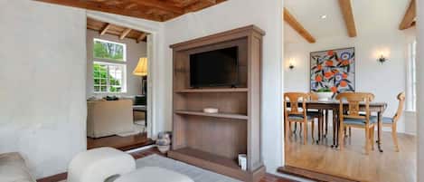 A living room with a TV, wooden furniture, and a dining area with a table and chairs.