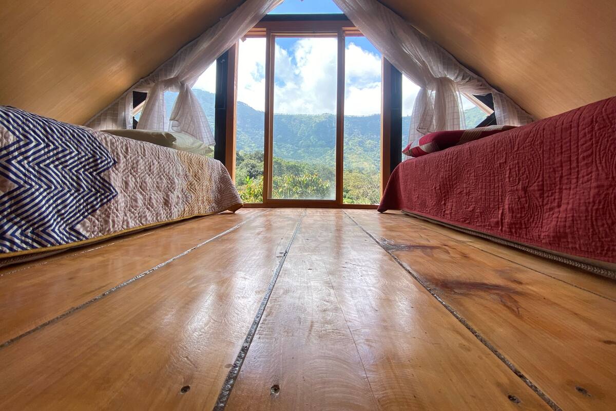 Un dormitorio acogedor en el ático con suelo de madera, dos camas con ropa de cama diferente y un gran ventanal con vistas a la montaña.