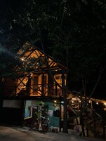 Una casa de madera rústica con estructura de techo triangular, rodeada de árboles y plantas en macetas.