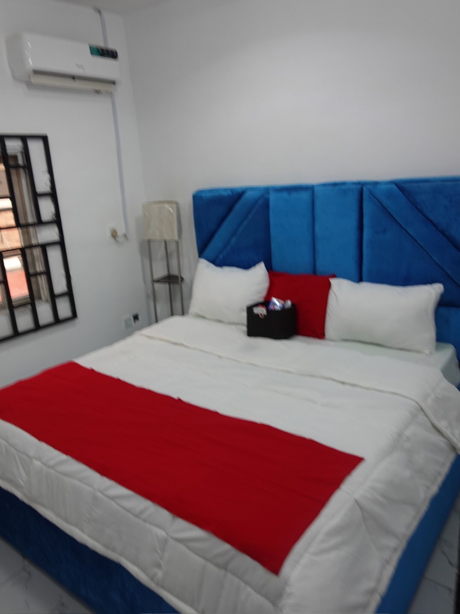 Een bed met een rode en witte dekbedovertrek, een blauw hoofdeinde en twee kussens.