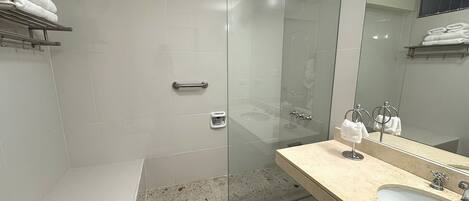 A modern bathroom with a glass-enclosed shower, a sink with a mirror, and neatly folded towels on a shelf.