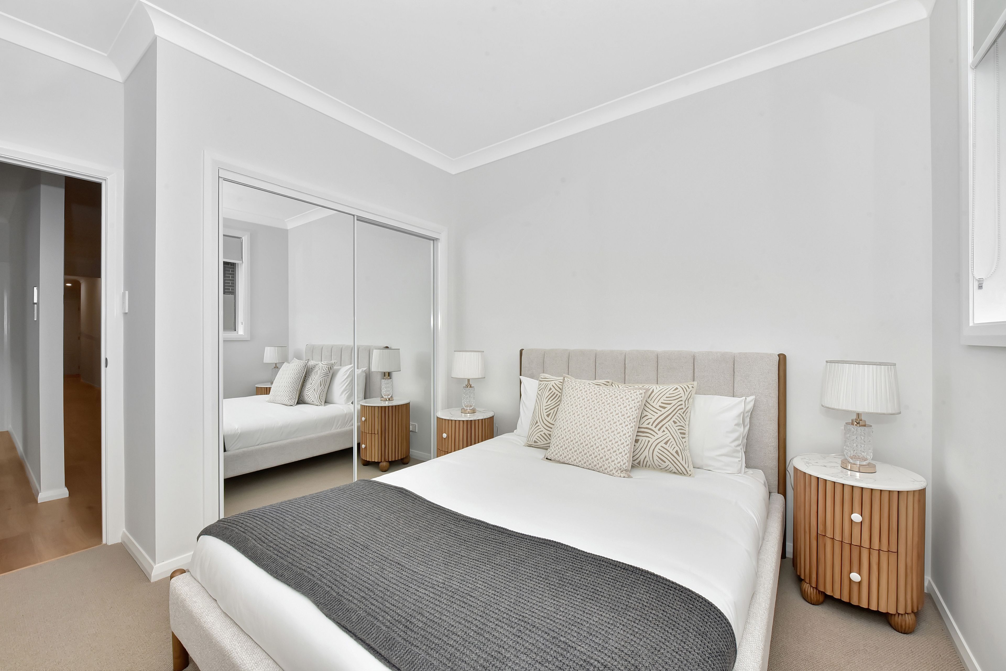 A modern bedroom with a large bed, two bedside tables, a mirror, and a wardrobe.