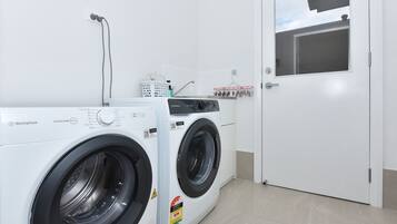 A laundry area with two white washing machines, a white door, and a window with a view of a building.
