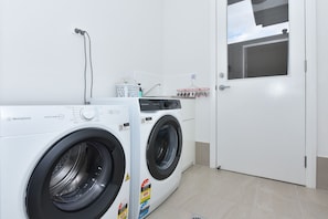 Une buanderie équipée de deux machines à laver blanches, une porte blanche et une fenêtre donnant sur un immeuble.
