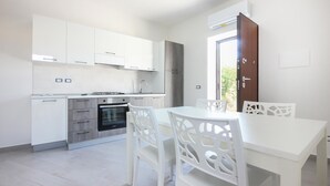 Cocina moderna con armarios blancos, horno empotrado y comedor con sillas y mesa blancos.