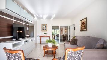 Uma sala de estar moderna com televisão de tela plana, um sofá, poltronas estampadas, uma mesa de madeira redonda com uma planta e obras de arte nas paredes.