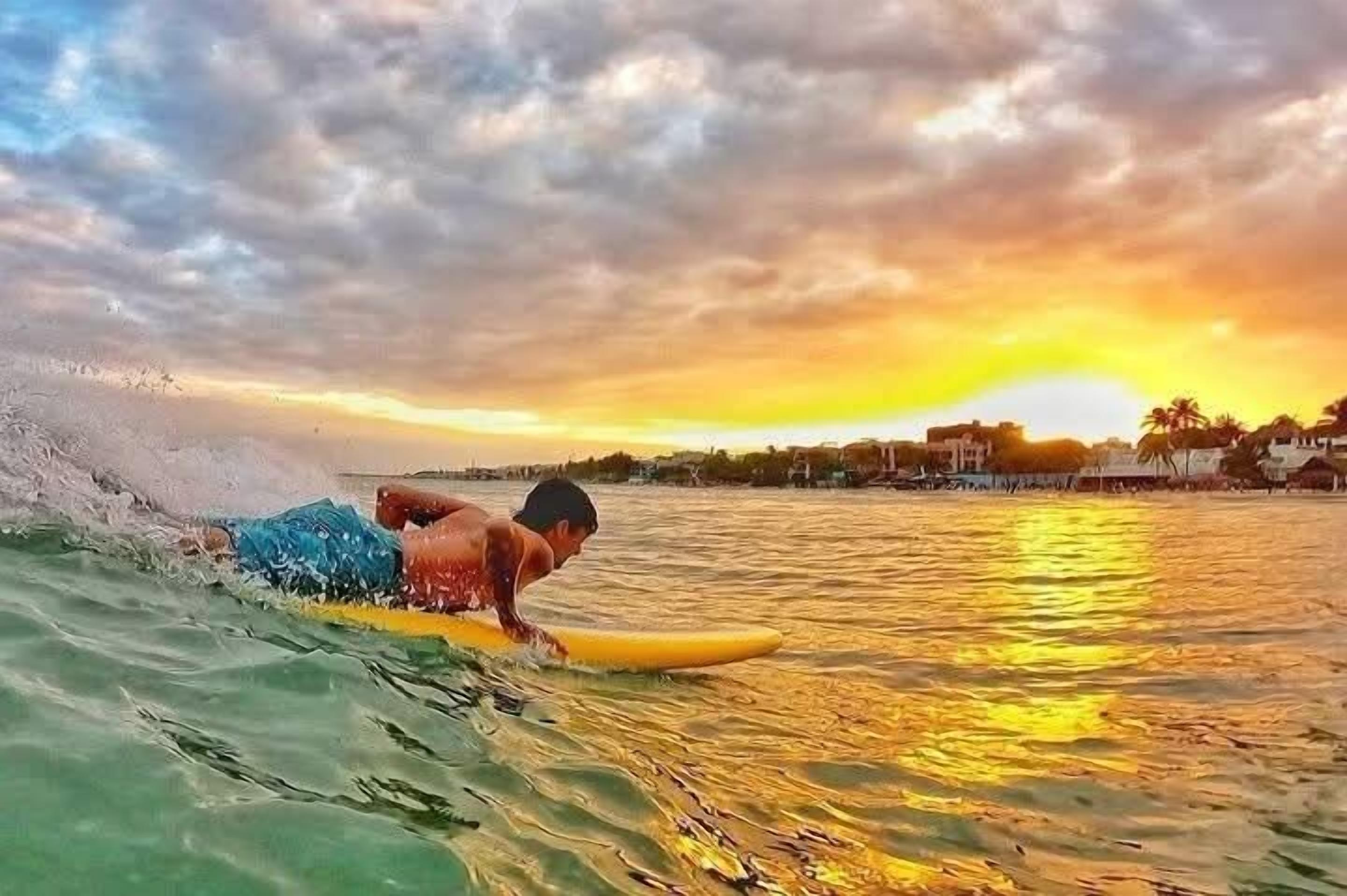 A person surfing on a yellow board in a body of water with a sunset in the background.
