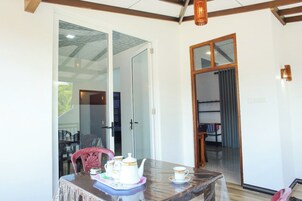 Un comedor con una mesa lista para el té, una silla y vistas del interior a través de un puerta de cristal.