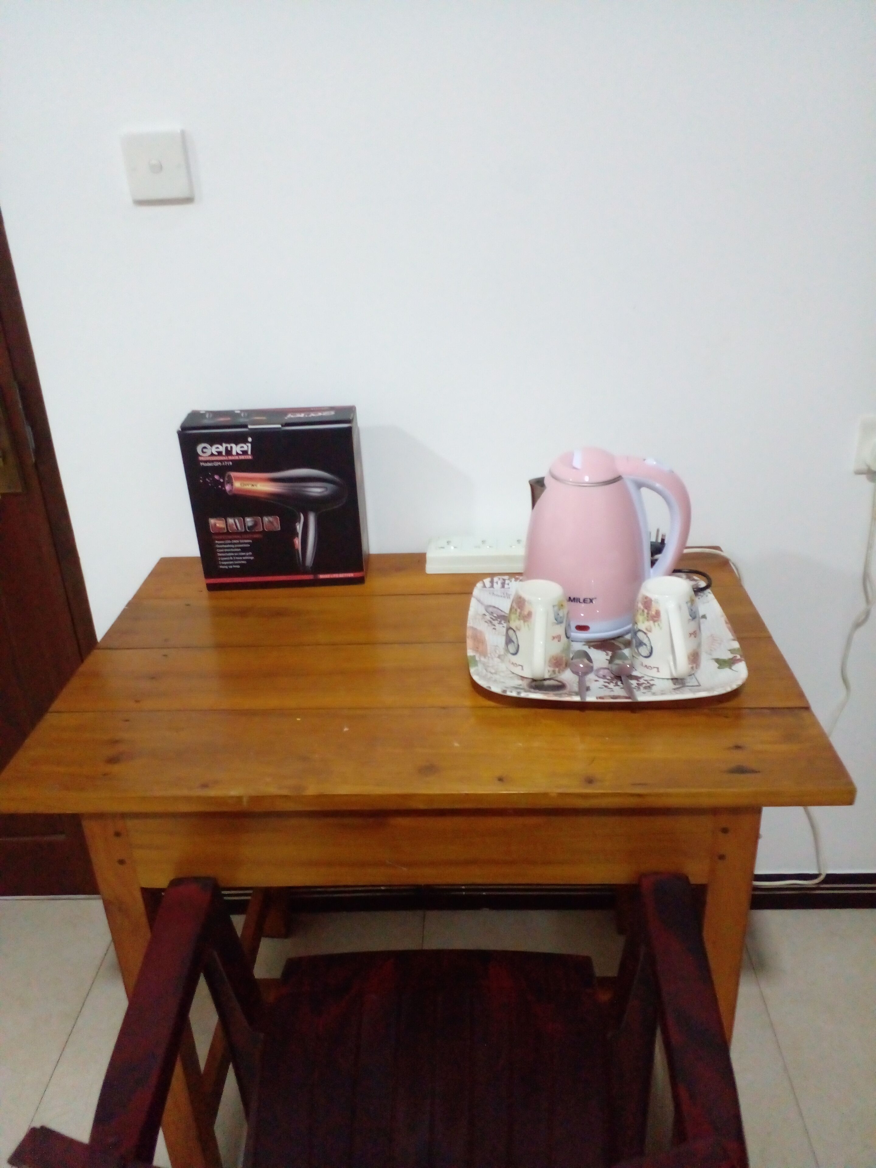 A wooden table with a box, a pink kettle, and two mugs on a floral coaster.