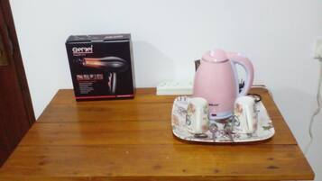A wooden table with a box, a pink kettle, and two mugs on a floral coaster.