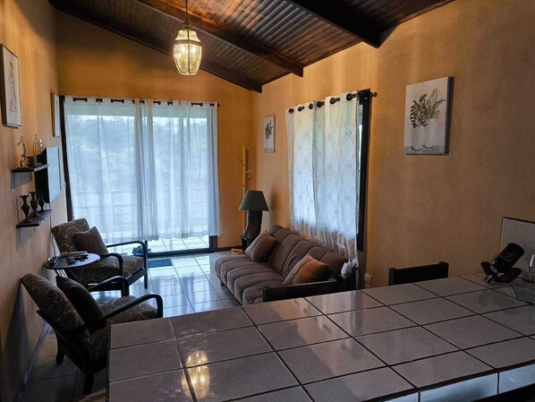Una sala de estar acogedora con sofá, sillones, una mesa baja de baldosas, una lámpara y una luz en el techo.