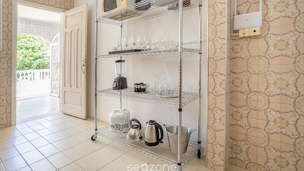 Une cuisine avec un meuble métallique servant d’étagère pour ranger les ustensiles de cuisine et les appareils électroménagers, un sol carrelé et un mur décoré d’un motif.