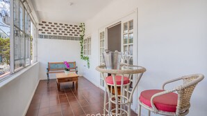 Un balcon avec un fauteuil en osier, une table en bois et un banc.