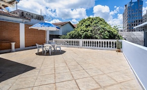 Un patio con piso de baldosas, barandilla blanca y una mesa con sillas.