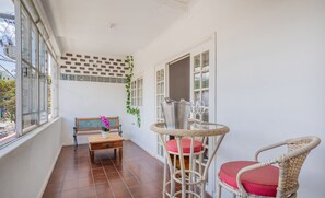 Un balcon avec un fauteuil en osier, une table en bois et un banc.