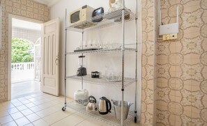 Une cuisine avec un meuble métallique servant d’étagère pour ranger les ustensiles de cuisine et les appareils électroménagers, un sol carrelé et un mur décoré d’un motif.