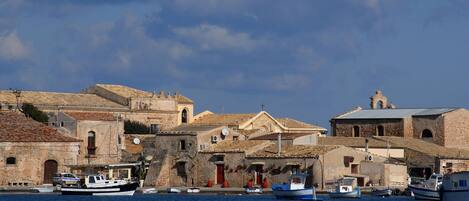 Une ville côtière dotée de bâtiments historiques, de bateaux amarrés le long du port et d’un ciel dégagé.