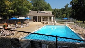 En swimmingpool med liggestole og parasoller, en overdækket terrasse og en bygning med en hegnede terrasse.