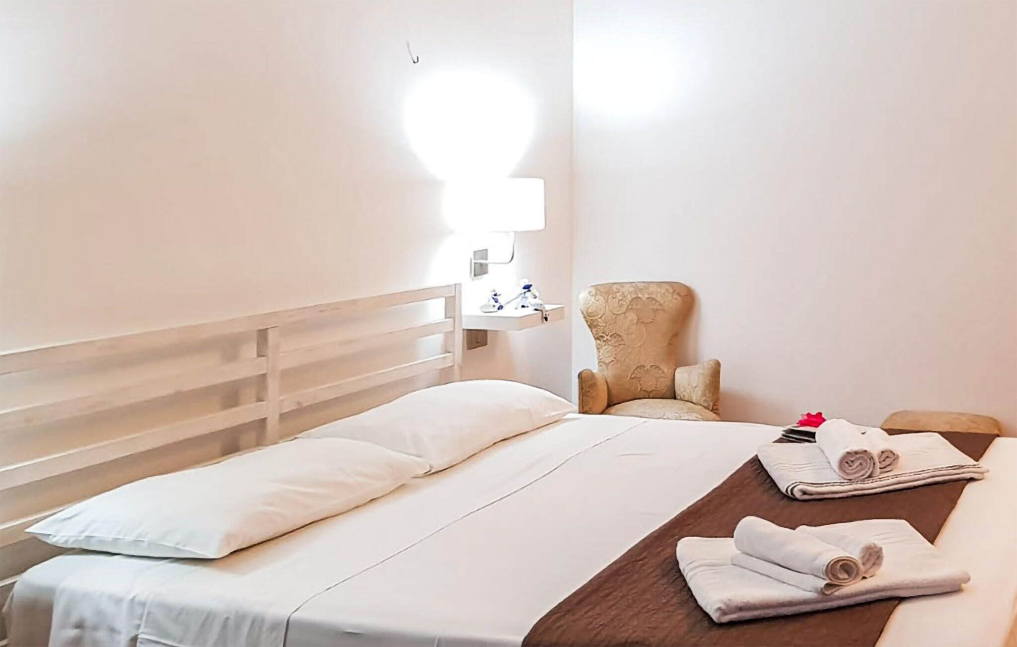 Une chambre d’hôtel avec un lit, une chaise, une table de chevet et une lampe.