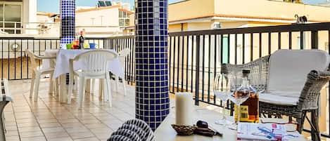A balcony with a table and chairs, a wicker sofa, and a railing.