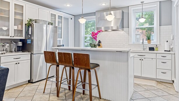 Una cocina moderna con armarios blancos, electrodomésticos de acero inoxidable y una isla central con taburetes de bar.