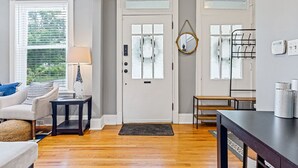 Un salón con una puerta blanca, una lámpara, un espejo y un banco.