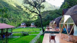 Ein Resort mit mehreren Geodätkuppel-Kabinen, einer zentralen Rasenfläche und einer Holzterrasse mit Sitzgelegenheiten.