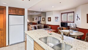 Una cocina con refrigerador, encimera de granito, lavamanos y comedor con mesa y sillas.