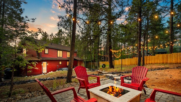 A backyard with a fire pit, red Adirondack chairs, and string lights. - Mountain Fun w/Hot Tub, Game Areas, Huge Yard, Waffle Bar! Pet Friendly (Flagstaff)
