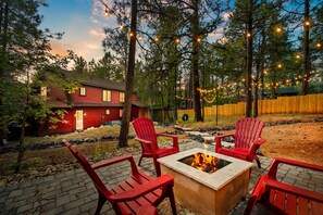A backyard with a fire pit, red Adirondack chairs, and string lights.