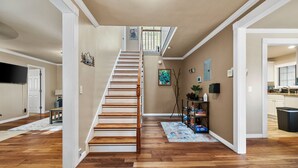 A spacious hallway with a wooden staircase leading to a second floor, a dining area, and a kitchen visible through an open door. - Mountain Fun w/Hot Tub, Game Areas, Huge Yard, Waffle Bar! Pet Friendly (Flagstaff)