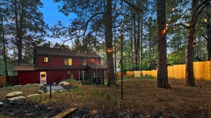 A red house with a visible garage door, surrounded by trees and a wooden fence. - Mountain Fun w/Hot Tub, Game Areas, Huge Yard, Waffle Bar! Pet Friendly (Flagstaff)
