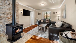 A living room with a black wood-burning stove, a leather sofa, a coffee table, and a brick wall. - Mountain Fun w/Hot Tub, Game Areas, Huge Yard, Waffle Bar! Pet Friendly (Flagstaff)