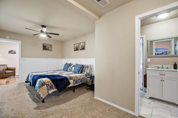 A bedroom with a bed, a ceiling fan, a door leading to a bathroom, and a small rug.