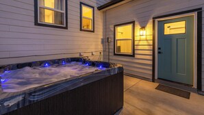 Een bubbelbad met blauwe LED-verlichting, een blauwe deur en twee verlichte ramen in de buitenmuur van een huis.