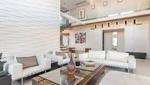 A modern living room with white sofas, a glass coffee table, and a staircase leading to an upper level.