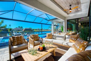 A modern outdoor lounge area with a pool view, furnished with sofas, chairs, and a coffee table. - VILLA GRAND BAY ROYALE – HEATED POOL & SPA | GULF ACCESS | BOAT RENTAL + TOURS VOUCHER INCL. (Cape Coral)
