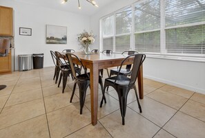 Ein Essbereich mit Holztisch und Stühlen, einer Blumenvase und einem Fenster mit Jalousien.