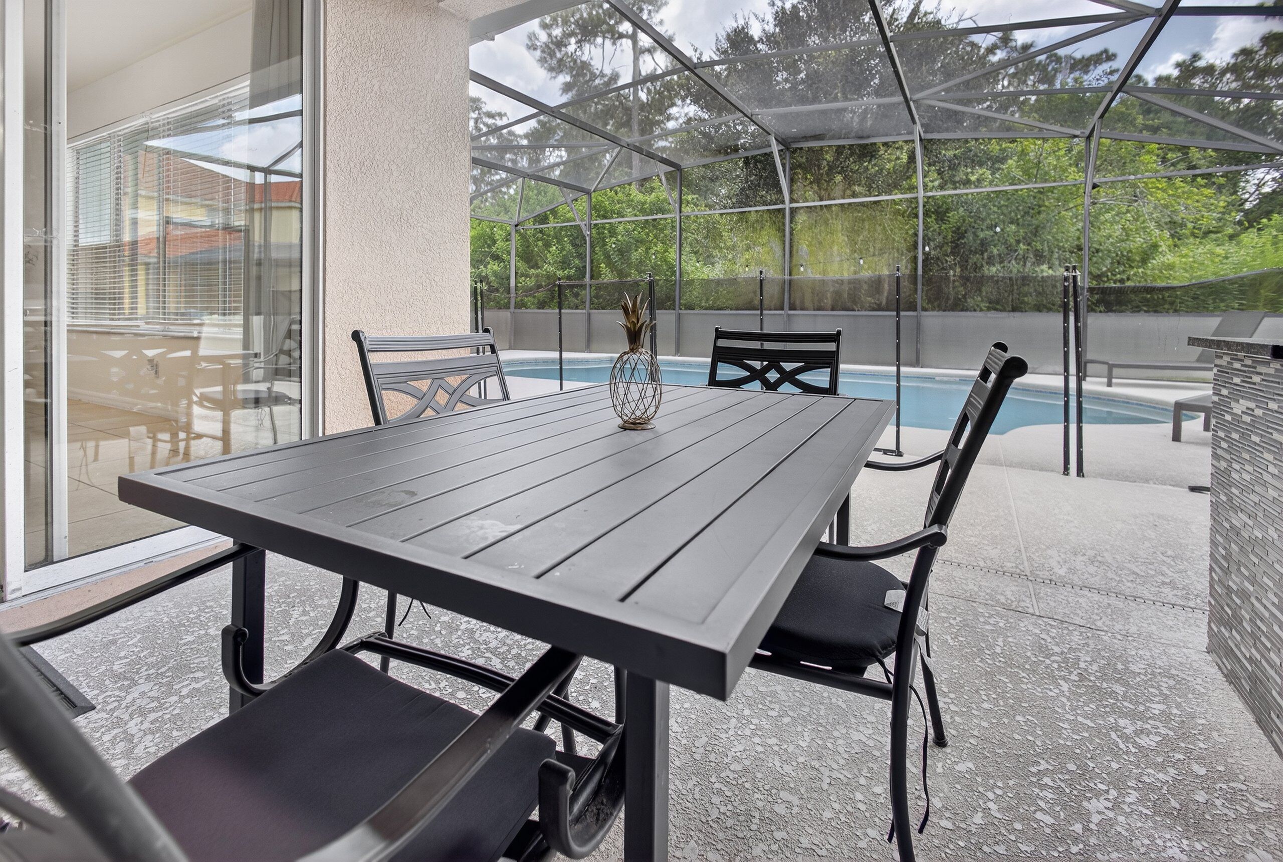 Un patio exterior con mesa y sillas, una piscina y un cerramiento de vidrio.