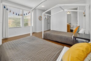 Un dormitorio con dos camas, un escritorio y un baño a la vista a través de una puerta abierta.