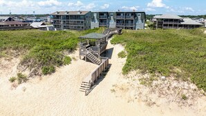 A beachfront hotel with a sandy walkway leading to a wooden deck. - Gone Coastal | Oceanfront | Community Pool (Kill Devil Hills)