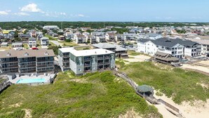 A coastal residential area with modern multi-story buildings, a swimming pool, and a beach access walkway. - Gone Coastal | Oceanfront | Community Pool (Kill Devil Hills)
